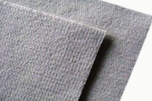 Close-up of gray needle-punched fabric folded over itself: a matte, felted surface showing the fine pitting left by the needles and the edge of the fold