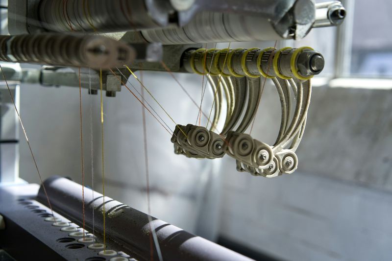 Detalle de una máquina textil: guías metálicas curvas y rodillos por los que pasan hilos finos tensados